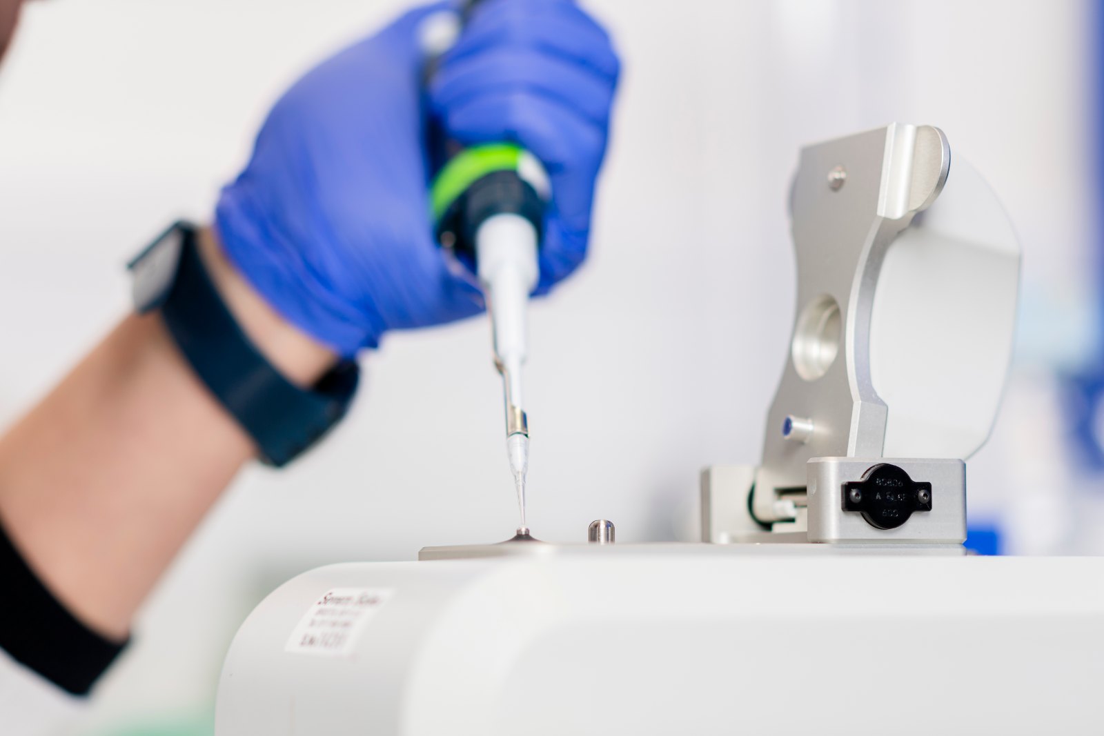 Mano con guante de nitrilo azul deposita con una micropipeta una muestra de ADN en un espectrofotómetro para medir su calidad
