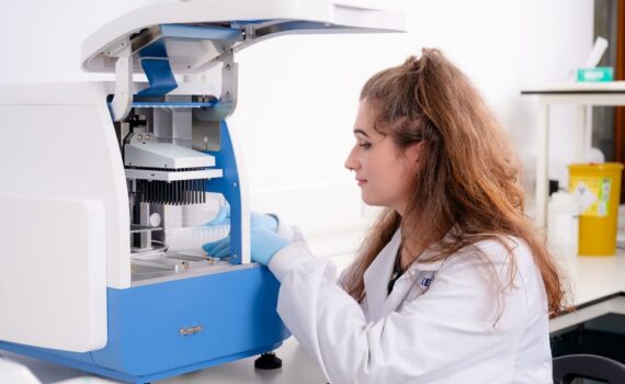 Técnica de laboratorio con bata blanca y guantes azules opera un equipo automatizado de extracción de ADN