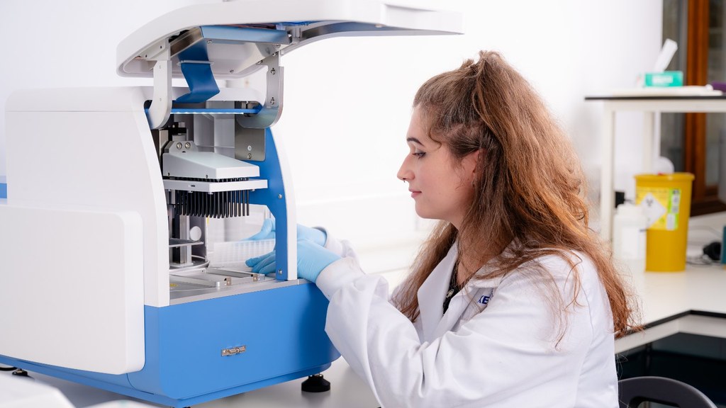 Técnica de laboratorio con bata blanca y guantes azules opera un equipo automatizado de extracción de ADN