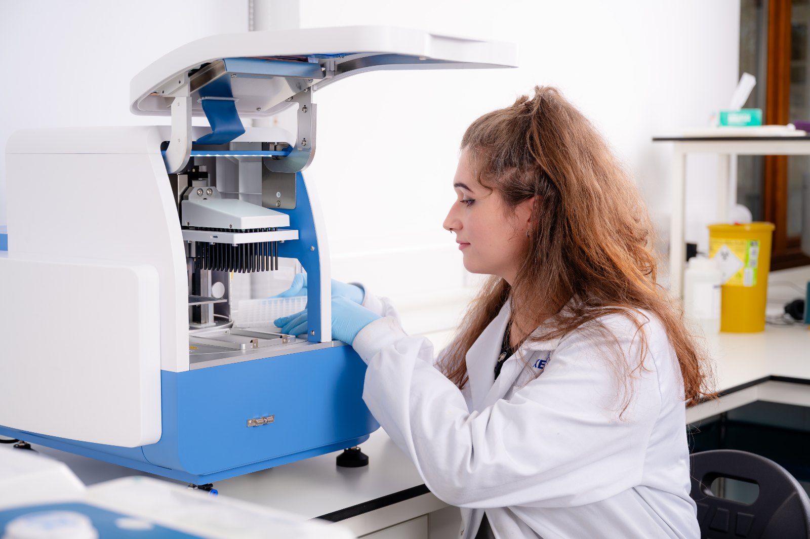 Técnica de laboratorio con bata blanca y guantes azules opera un equipo automatizado de extracción de ADN