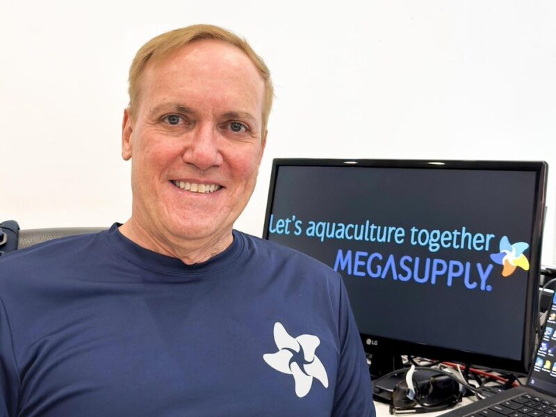 José Ignacio Curiel, CEO de Megasupply, sonríe con camiseta azul marino con el logotipo de la empresa, junto a un monitor que muestra el lema Let's aquaculture together y la marca Megasupply